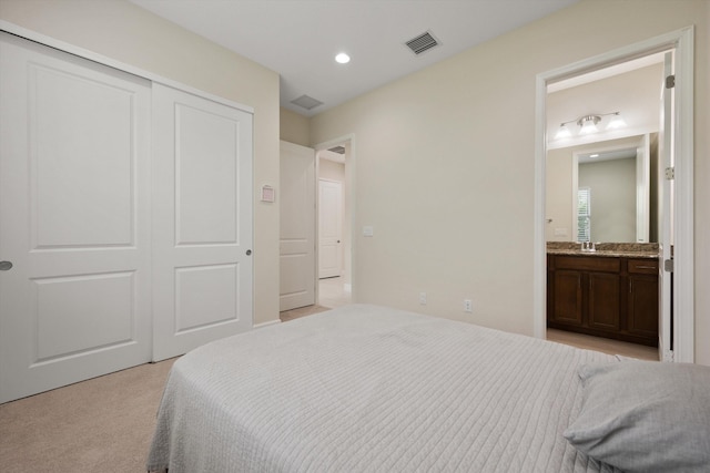 bedroom with ensuite bathroom, sink, light carpet, and a closet