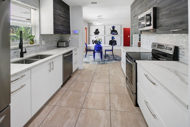 kitchen featuring backsplash, appliances with stainless steel finishes, light stone countertops, sink, and white cabinets