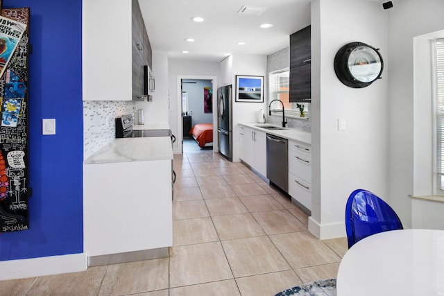 kitchen with tasteful backsplash, stainless steel appliances, white cabinetry, light tile patterned floors, and sink