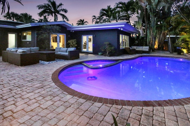 pool at dusk featuring an in ground hot tub, an outdoor living space, and a patio area