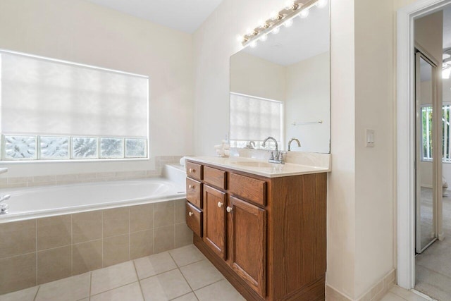 bathroom with tile patterned floors, tiled tub, a wealth of natural light, and vanity