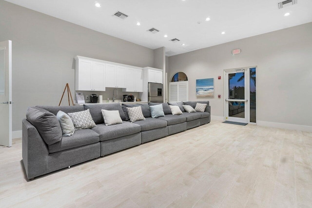 living room featuring sink, a high ceiling, and light hardwood / wood-style flooring