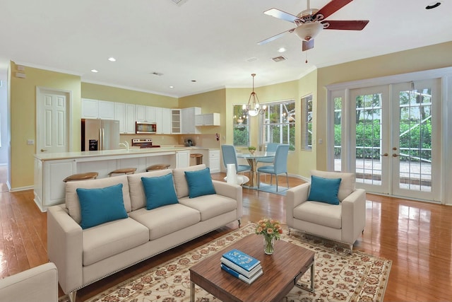 living room featuring french doors, ceiling fan with notable chandelier, sink, ornamental molding, and light hardwood / wood-style floors