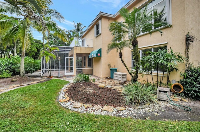 back of property featuring a lawn, glass enclosure, and a balcony