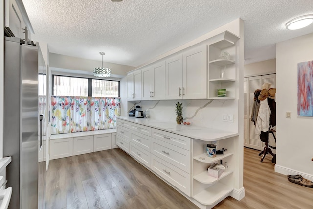 kitchen featuring stainless steel fridge, white cabinetry, decorative light fixtures, a textured ceiling, and light hardwood / wood-style floors