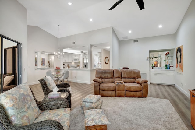 living room with ceiling fan with notable chandelier, light hardwood / wood-style flooring, and high vaulted ceiling