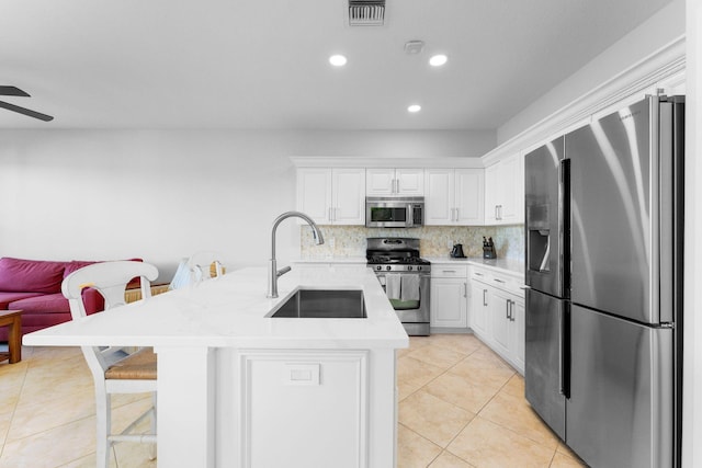 kitchen with a kitchen breakfast bar, tasteful backsplash, stainless steel appliances, sink, and white cabinetry