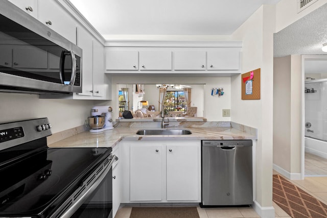 kitchen with sink, white cabinets, light tile patterned floors, light stone counters, and stainless steel appliances