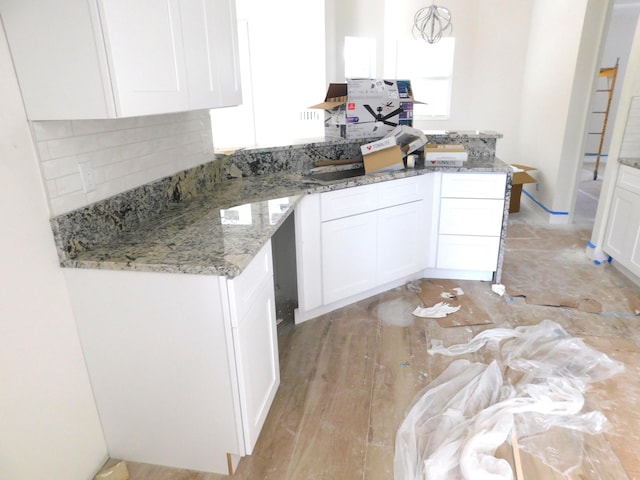 kitchen with decorative backsplash, light stone counters, light hardwood / wood-style flooring, white cabinetry, and hanging light fixtures