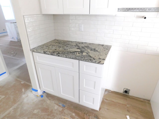 kitchen featuring backsplash, light stone countertops, and white cabinets