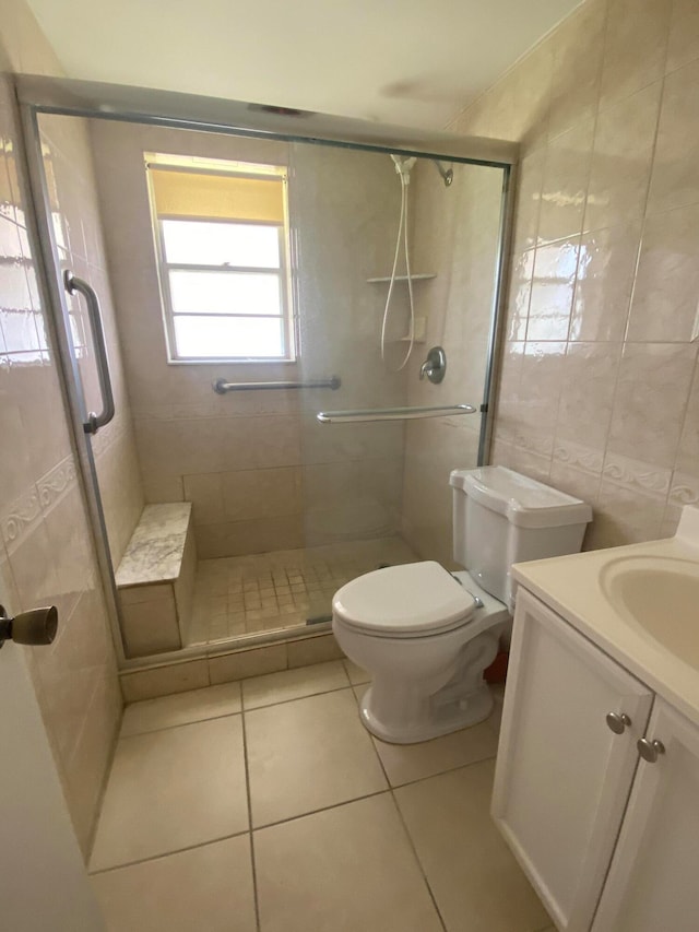 bathroom with tile walls, tile patterned floors, a shower with door, vanity, and toilet