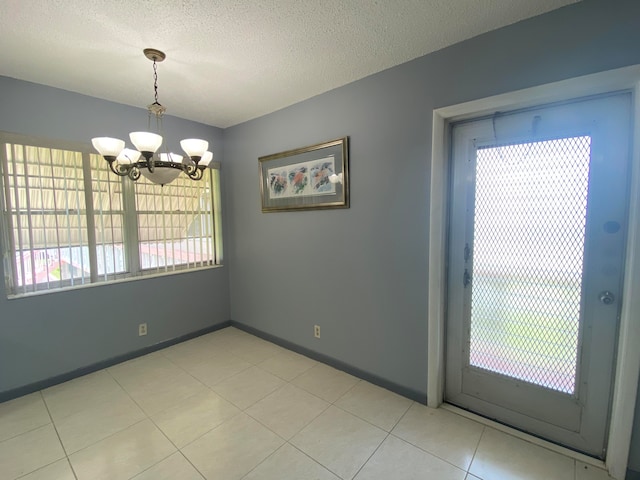 unfurnished dining area with a chandelier, a textured ceiling, and light tile patterned floors