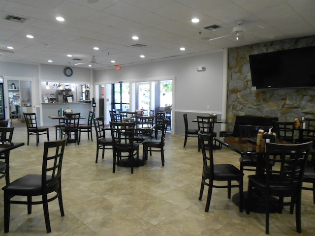 tiled dining space with a stone fireplace, a paneled ceiling, and ceiling fan