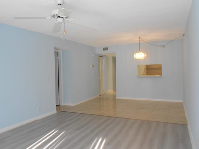 empty room with ceiling fan with notable chandelier and light hardwood / wood-style floors