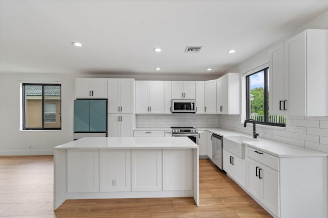 kitchen featuring light hardwood / wood-style floors, sink, a kitchen island, white cabinetry, and appliances with stainless steel finishes