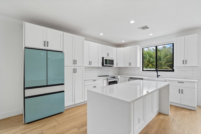 kitchen featuring sink, appliances with stainless steel finishes, a kitchen island, white cabinets, and light wood-type flooring