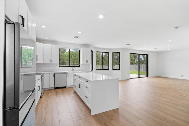 kitchen with stainless steel appliances, light hardwood / wood-style floors, white cabinets, and a kitchen island