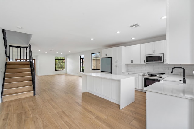 kitchen with light wood-type flooring, white cabinets, sink, and stainless steel appliances