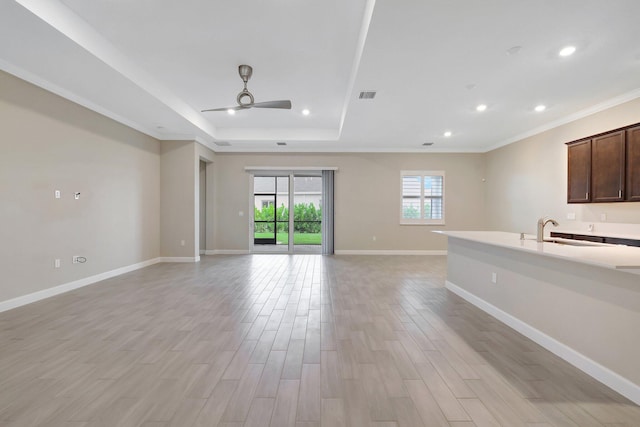 unfurnished living room featuring light hardwood / wood-style floors, sink, ceiling fan, a raised ceiling, and crown molding