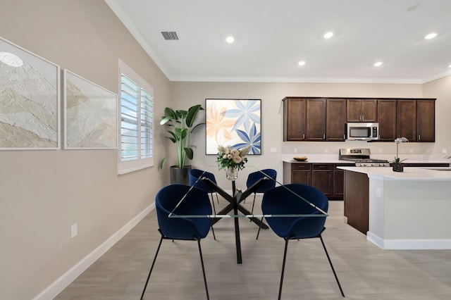 kitchen featuring ornamental molding, appliances with stainless steel finishes, dark brown cabinets, an island with sink, and light hardwood / wood-style flooring