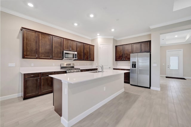 kitchen with stainless steel appliances, a center island with sink, sink, ornamental molding, and light hardwood / wood-style flooring