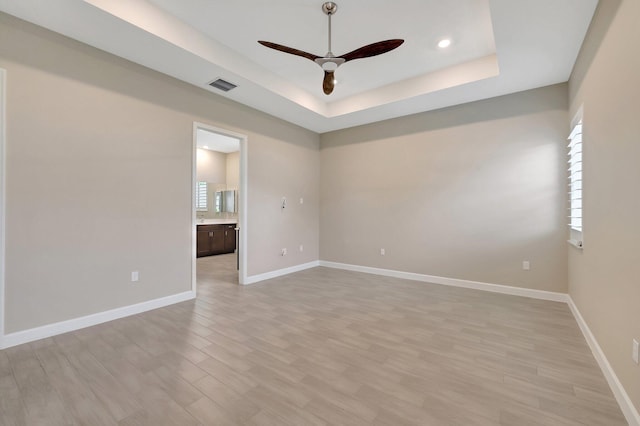 unfurnished room featuring ceiling fan, a raised ceiling, and light wood-type flooring