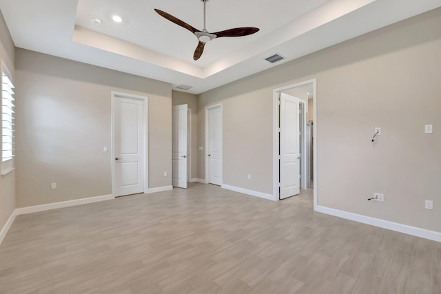 unfurnished bedroom featuring light wood-type flooring, ceiling fan, and a tray ceiling