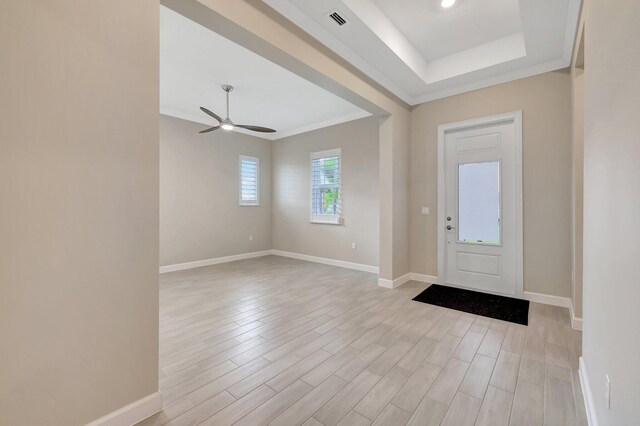 entrance foyer with ornamental molding, light hardwood / wood-style flooring, ceiling fan, and a raised ceiling