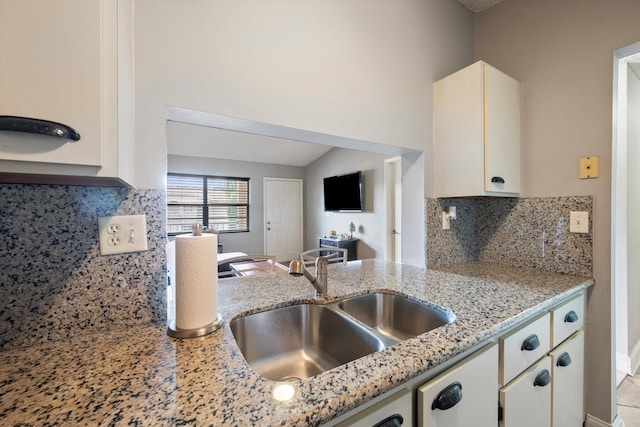 kitchen featuring tasteful backsplash, white cabinetry, sink, and light stone countertops