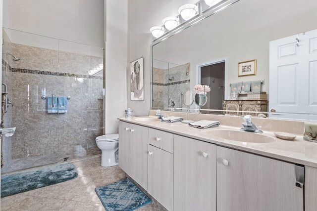 bathroom with toilet, vanity, tile patterned flooring, and a tile shower