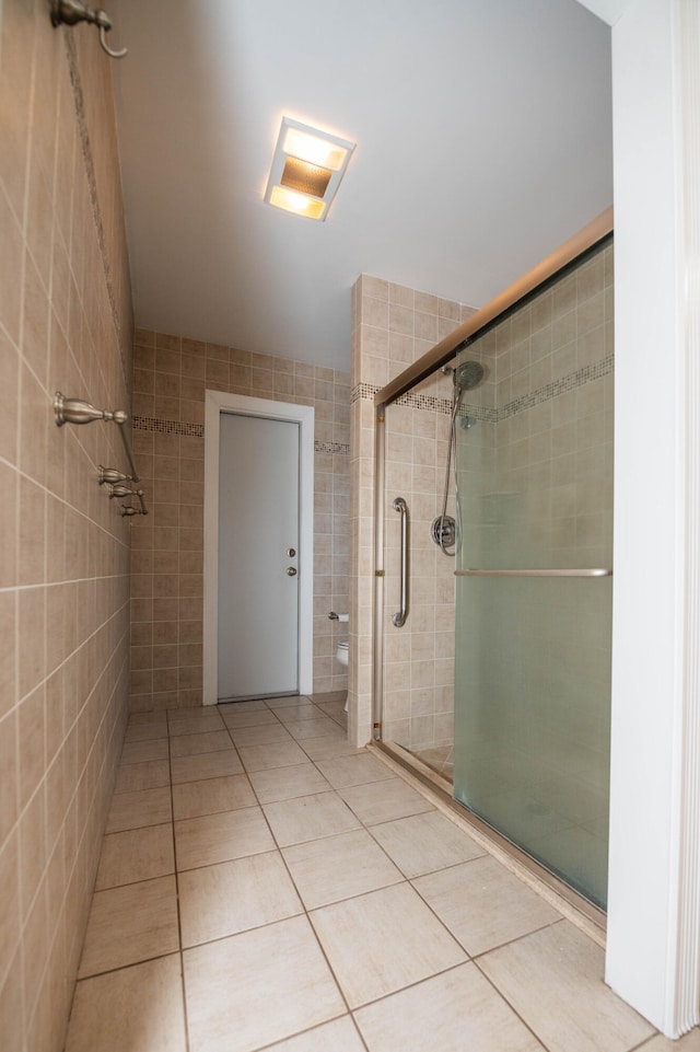 bathroom featuring tile patterned flooring, a shower with shower door, and tile walls