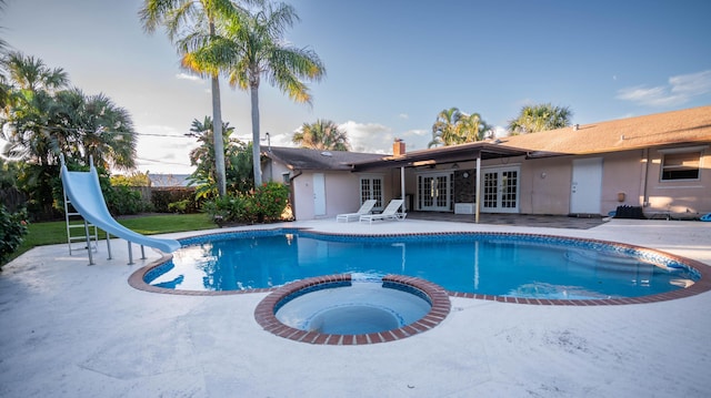 view of pool featuring fence, a water slide, a pool with connected hot tub, french doors, and a patio area