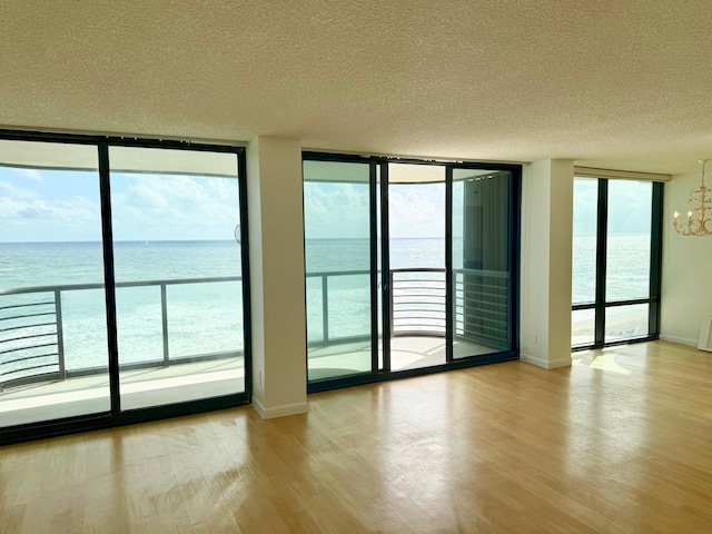 doorway featuring a water view, light wood-type flooring, a notable chandelier, and a textured ceiling