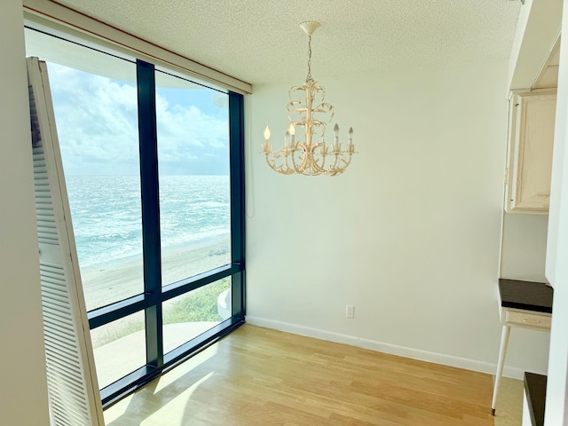 unfurnished dining area featuring a water view, light wood-type flooring, a notable chandelier, and a textured ceiling