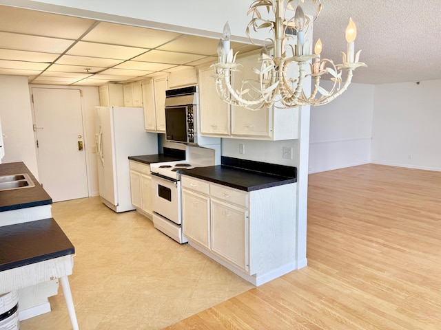 kitchen featuring a notable chandelier, white appliances, pendant lighting, a drop ceiling, and sink