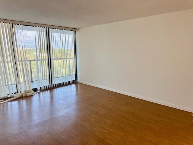 empty room with a textured ceiling, dark wood-type flooring, and a wall of windows