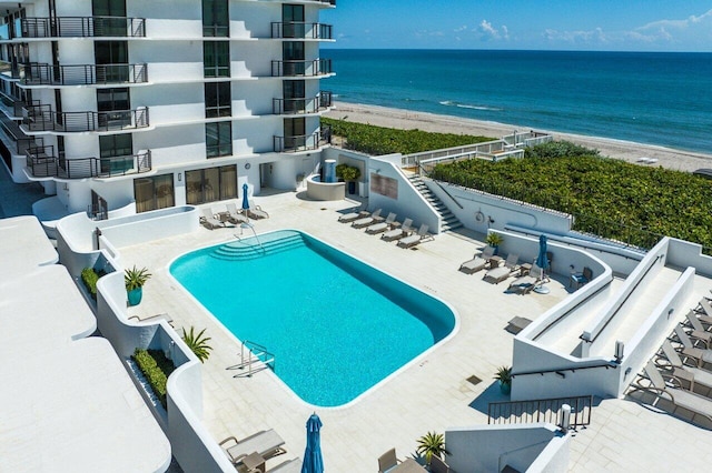 view of pool featuring a water view, a patio, and a beach view