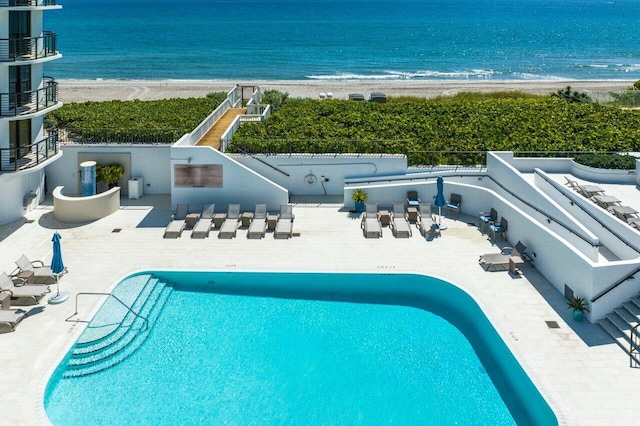 view of swimming pool with a patio area, a water view, and a view of the beach