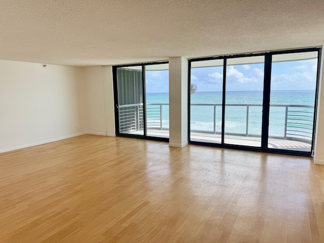 empty room with a textured ceiling, a healthy amount of sunlight, a water view, and light wood-type flooring