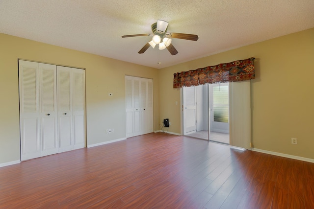 unfurnished bedroom featuring ceiling fan, wood-type flooring, a textured ceiling, and two closets