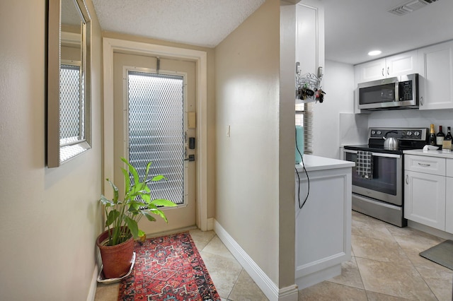 kitchen with light tile patterned floors, white cabinets, stainless steel appliances, and a textured ceiling