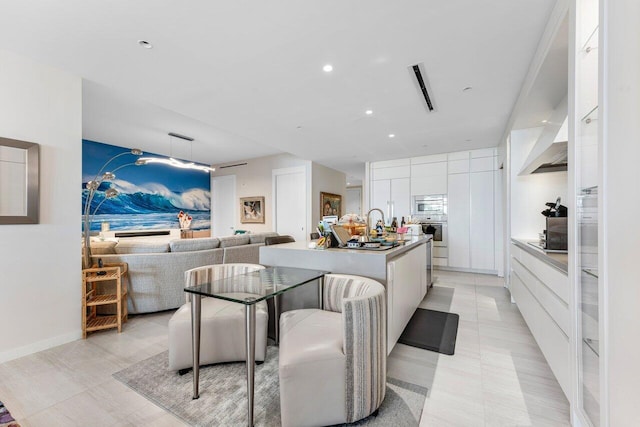 kitchen featuring stainless steel appliances, white cabinets, light tile patterned floors, a kitchen island with sink, and a breakfast bar