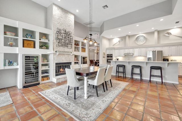 tiled dining room with a fireplace, a high ceiling, wine cooler, and built in shelves