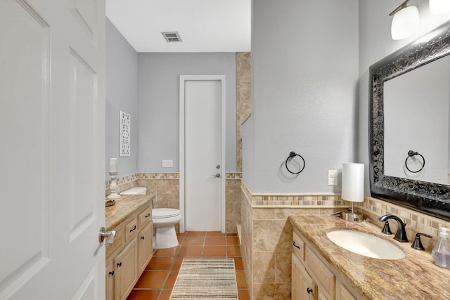 bathroom featuring tile patterned flooring, vanity, toilet, and tile walls