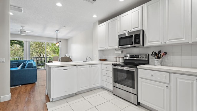 kitchen with white cabinetry, kitchen peninsula, appliances with stainless steel finishes, and pendant lighting