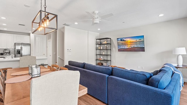 living room with light hardwood / wood-style floors and ceiling fan with notable chandelier