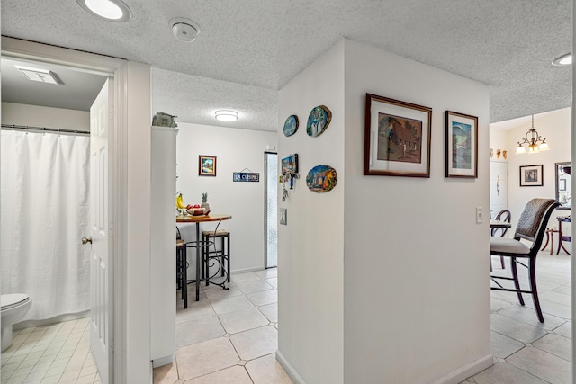 corridor featuring a textured ceiling, a notable chandelier, and light tile patterned floors