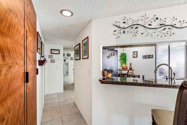 hallway with a textured ceiling and light tile patterned floors