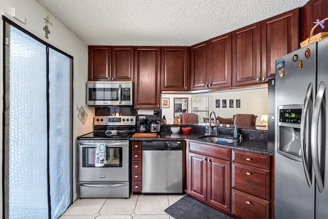 kitchen with stainless steel appliances, light tile patterned flooring, sink, dark stone countertops, and a textured ceiling