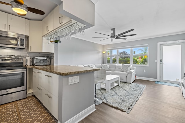 kitchen with stainless steel appliances, dark wood-type flooring, dark stone counters, kitchen peninsula, and tasteful backsplash